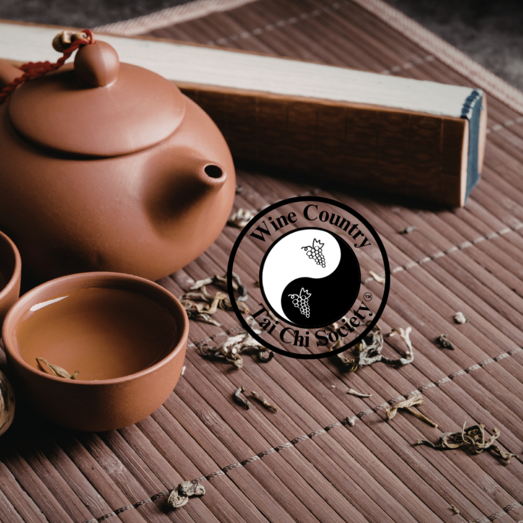 clay tea pot and cup with tea on a mat, with Tai Chi logo in center