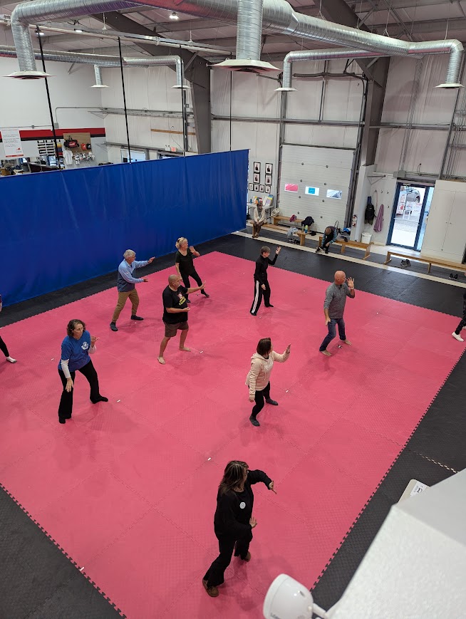 gym with mats and a dozen people doing Tai Chi